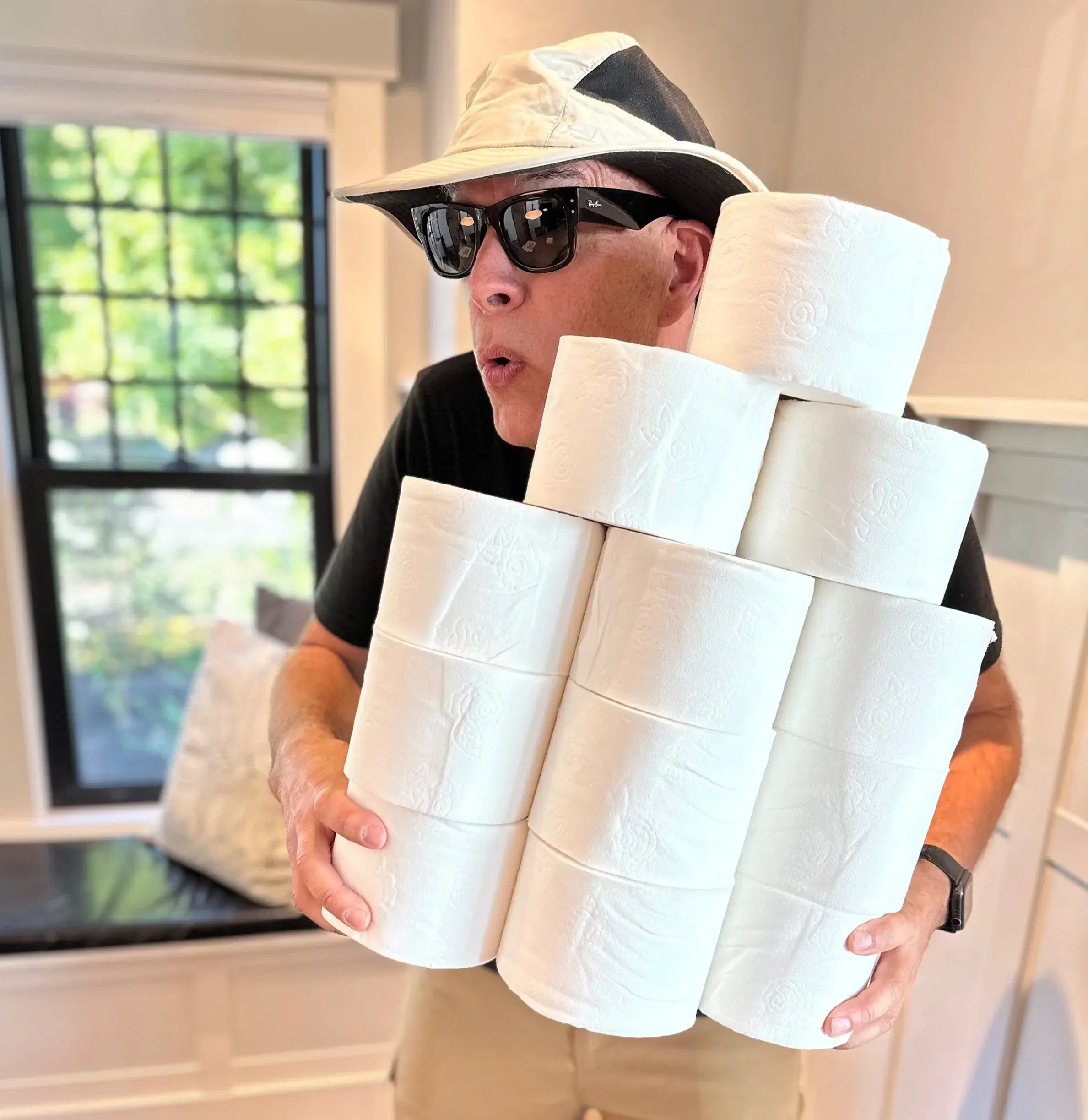 A guest in a sun hat and sunglasses carrying an armload of toilet paper rolls out of a rental.