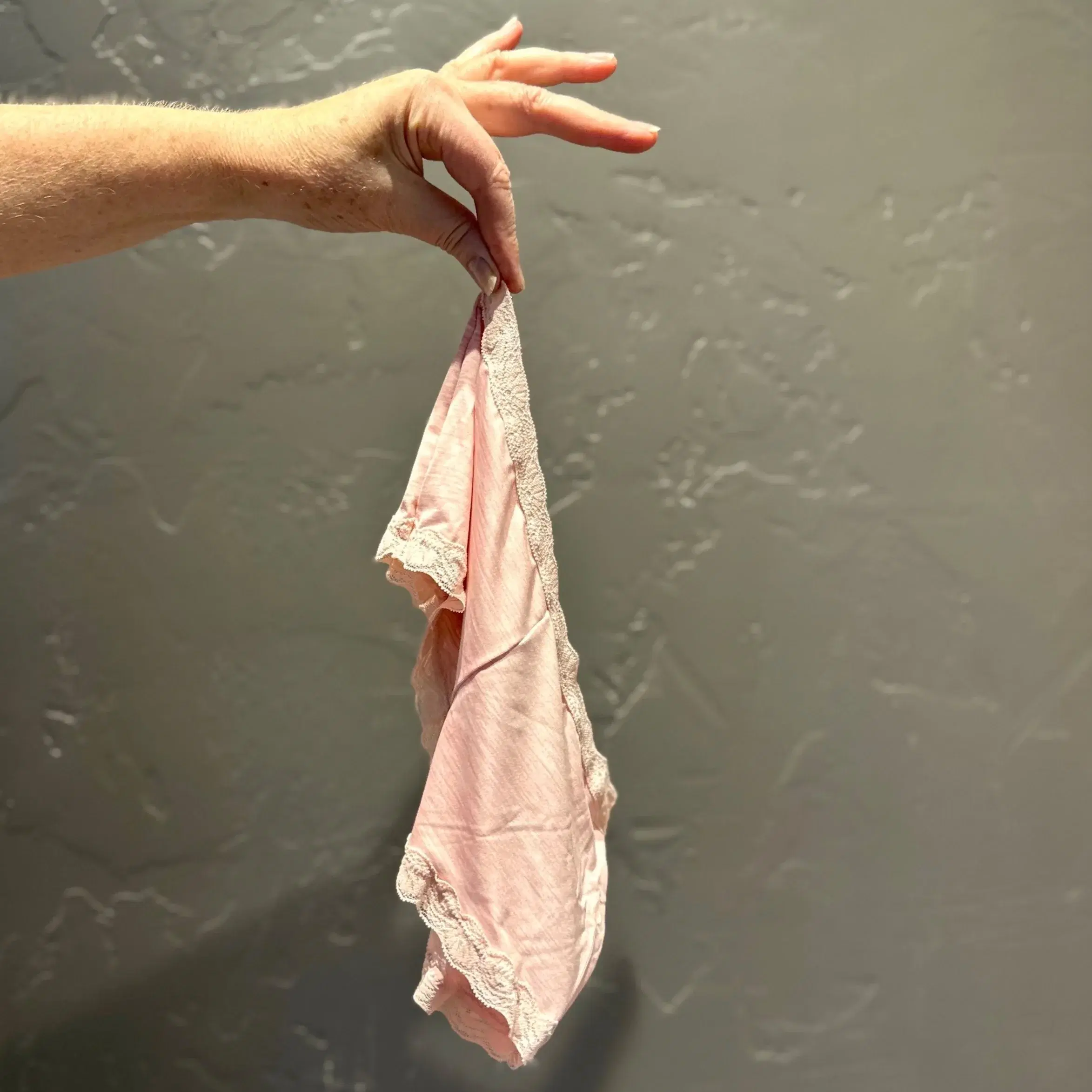 A hand dangling a pair of pink lace underwear left behind by a guest.