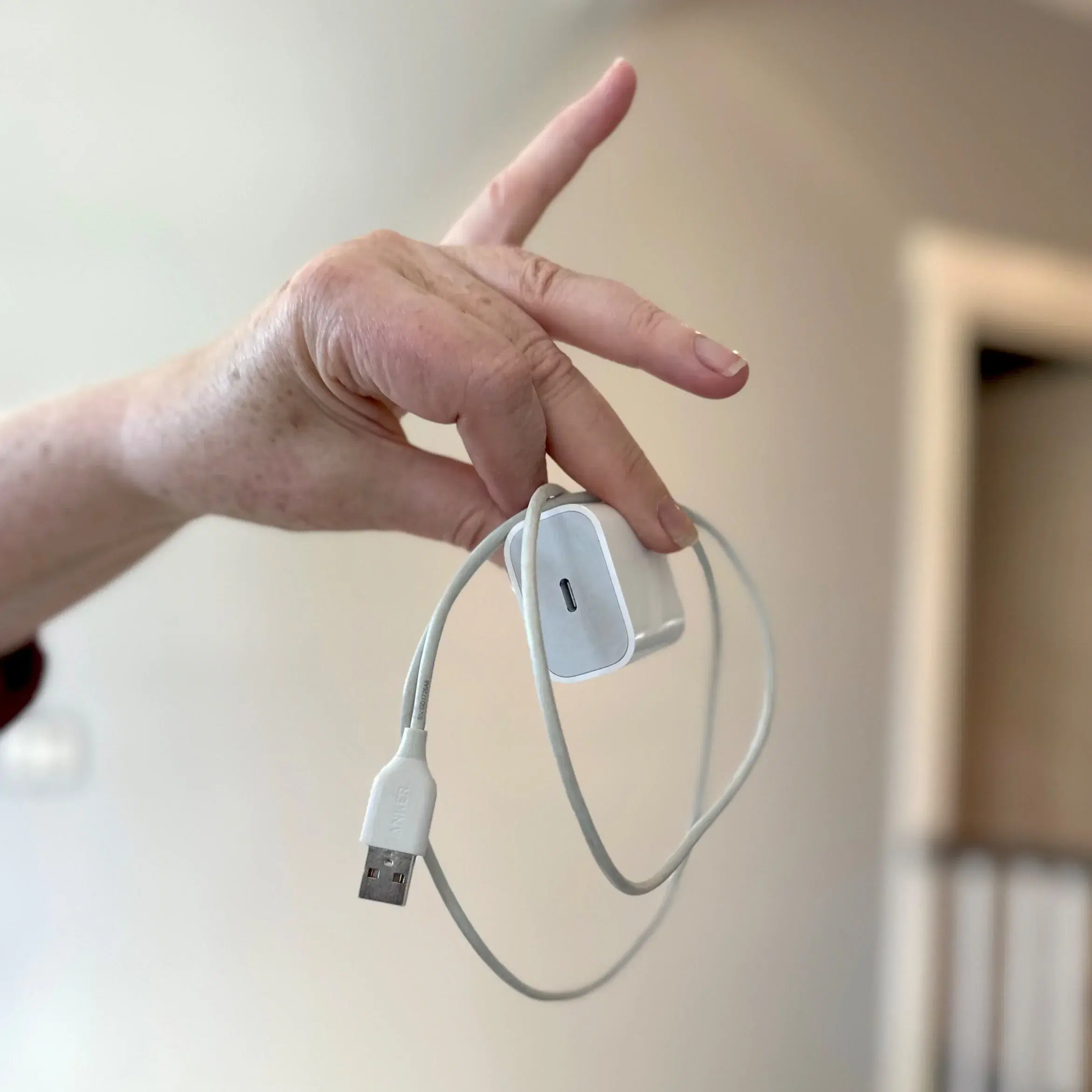 A hand holding a white phone charger and cable left behind by a guest.